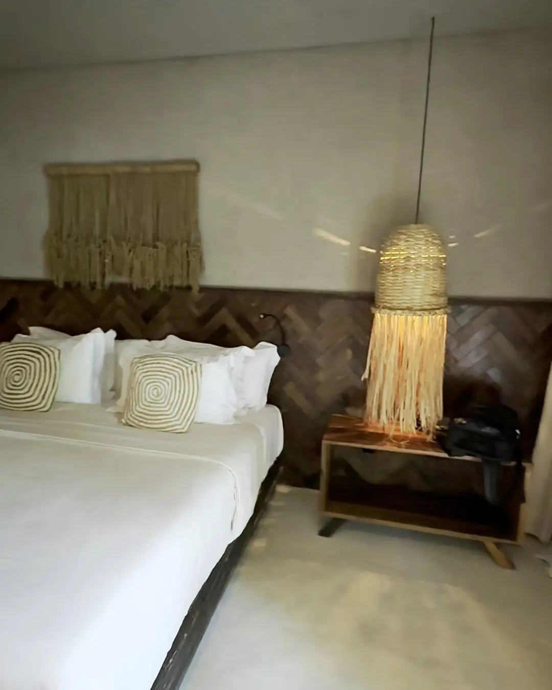 Quarto do bangalô do Zai Patacho, com cama de casal, parede de madeira e luminária de palha