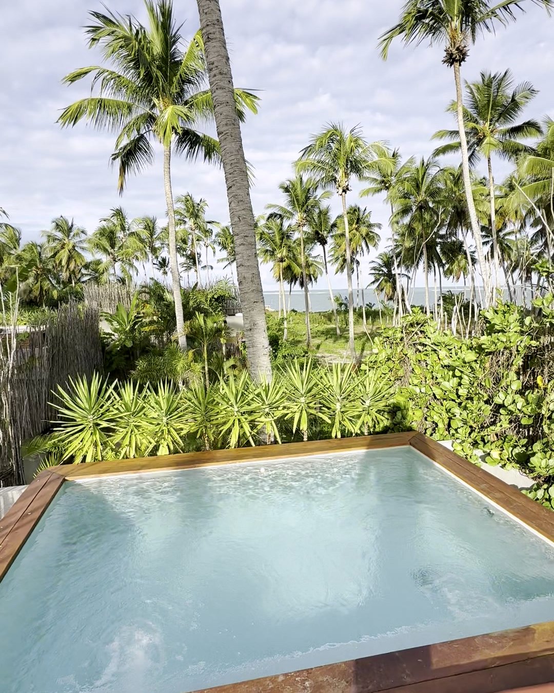 Piscina privativa do bangalô do Zai Patacho, com deck de madeira, coqueiral e o mar ao fundo